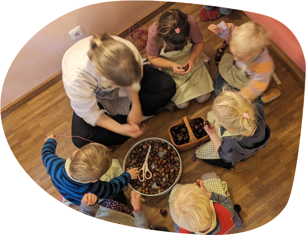 Eingewöhnung 5 Kinder und eine Erwachsene von oben. Zwischen den Personen stehen Schalen mit Kastanien.
