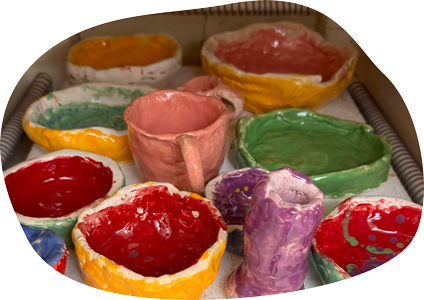 Töpfern_2 Auf einer Fläche stehen viele bunte Gefäße, die offenbar von Kindern hergestellt und glasiert wurden.