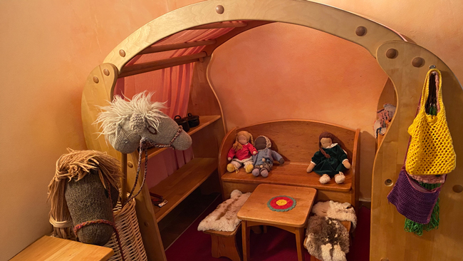 Puppenecke_kl Eine Holzkonstruktion, etwas wie ein Puppenhaus, oder Spielhütte nur im Innenbereich, mit Spielzeug, Puppen, Steckenpferden - Tisch und Bänken
